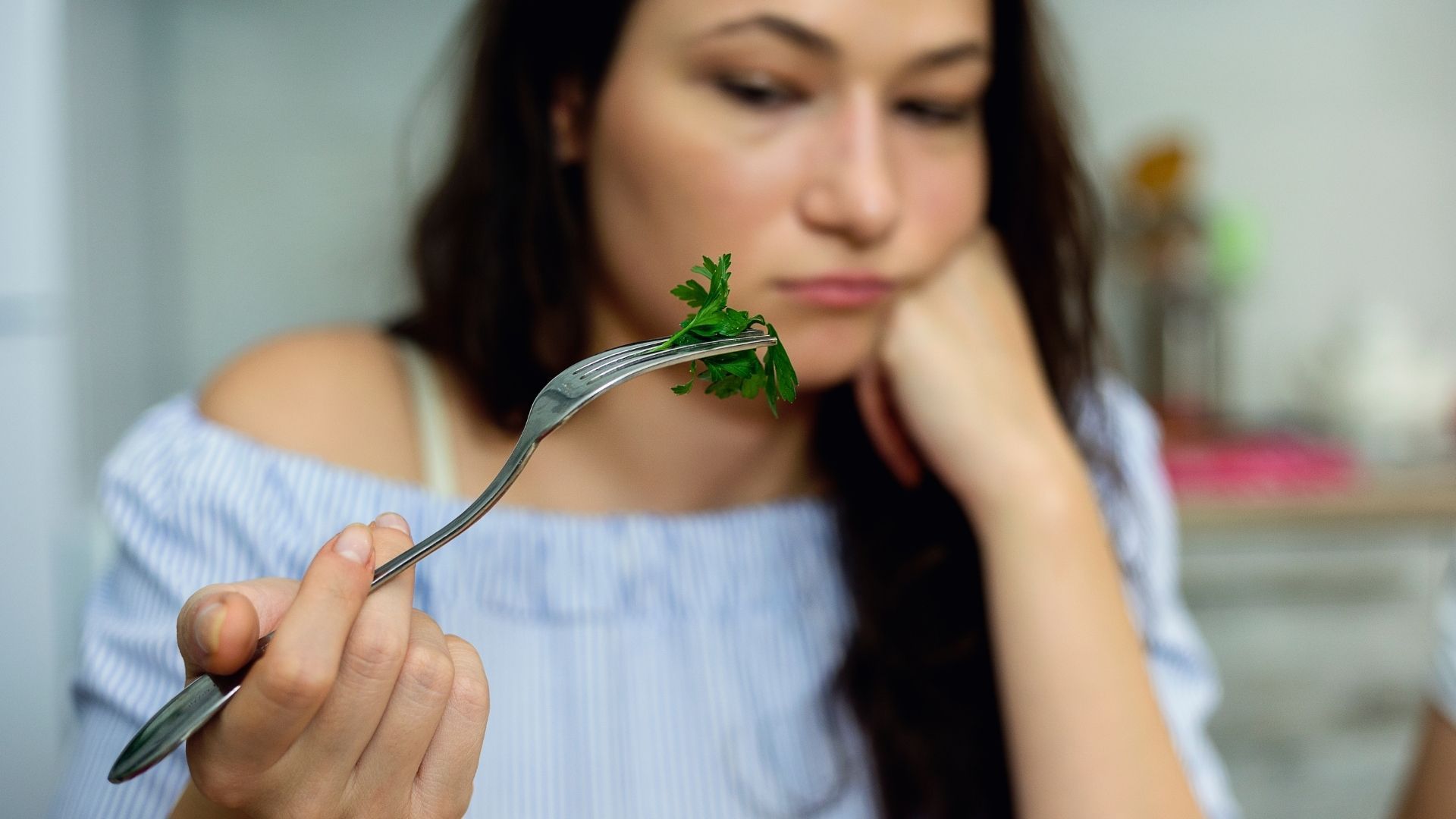 A woman is holding a fork with a piece of parsley on it.