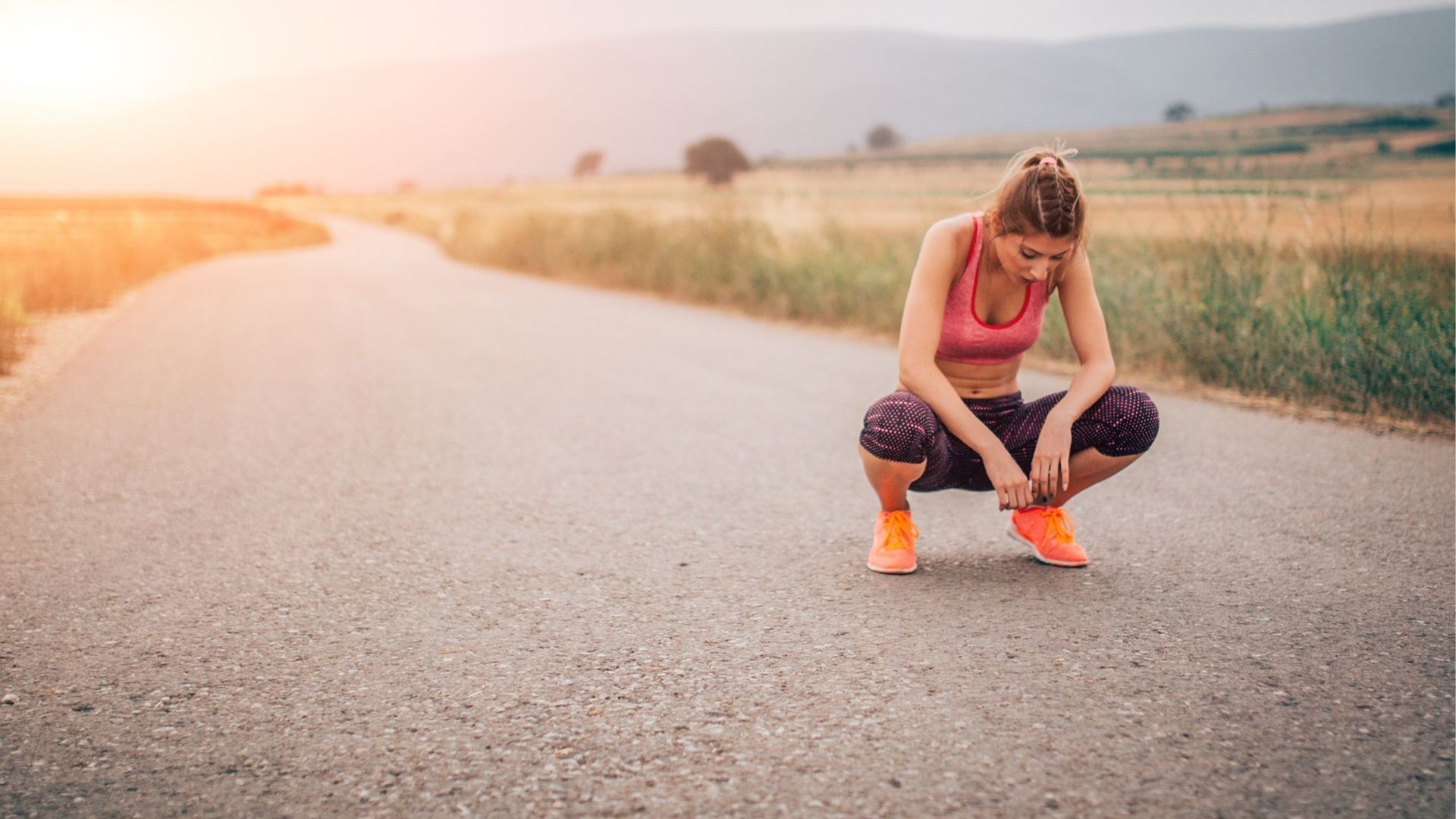 A woman is kneeling down on the side of a road tying her shoes.