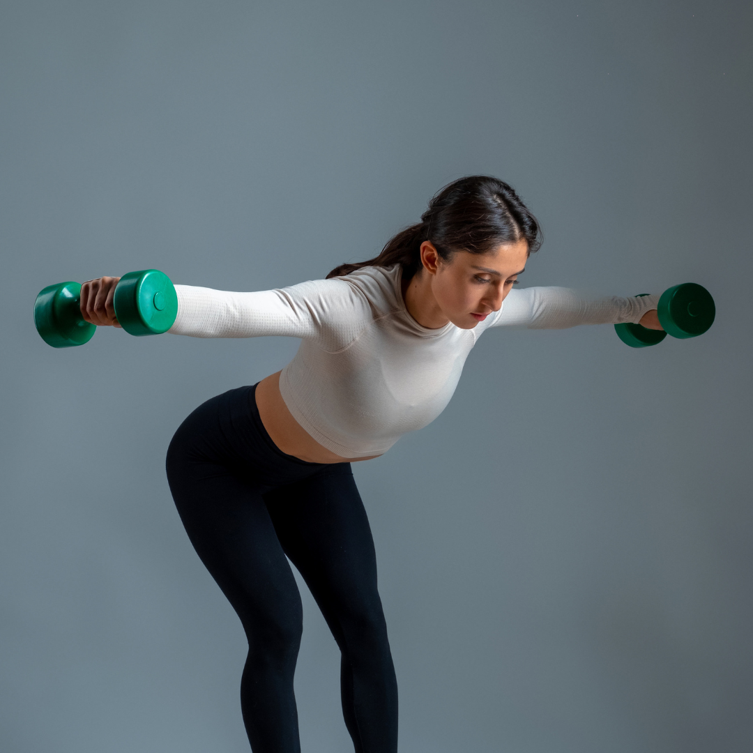 A woman is lifting green dumbbells with her arms outstretched. Strength Training and Nutritional Coaching