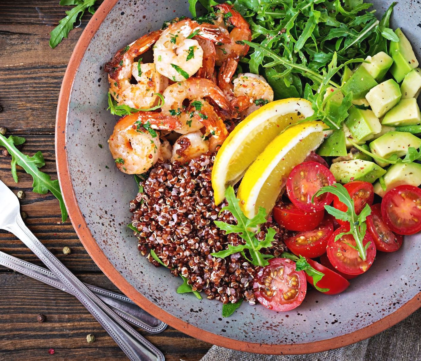 A bowl of food with shrimp , rice , tomatoes , avocado and lemon slices.