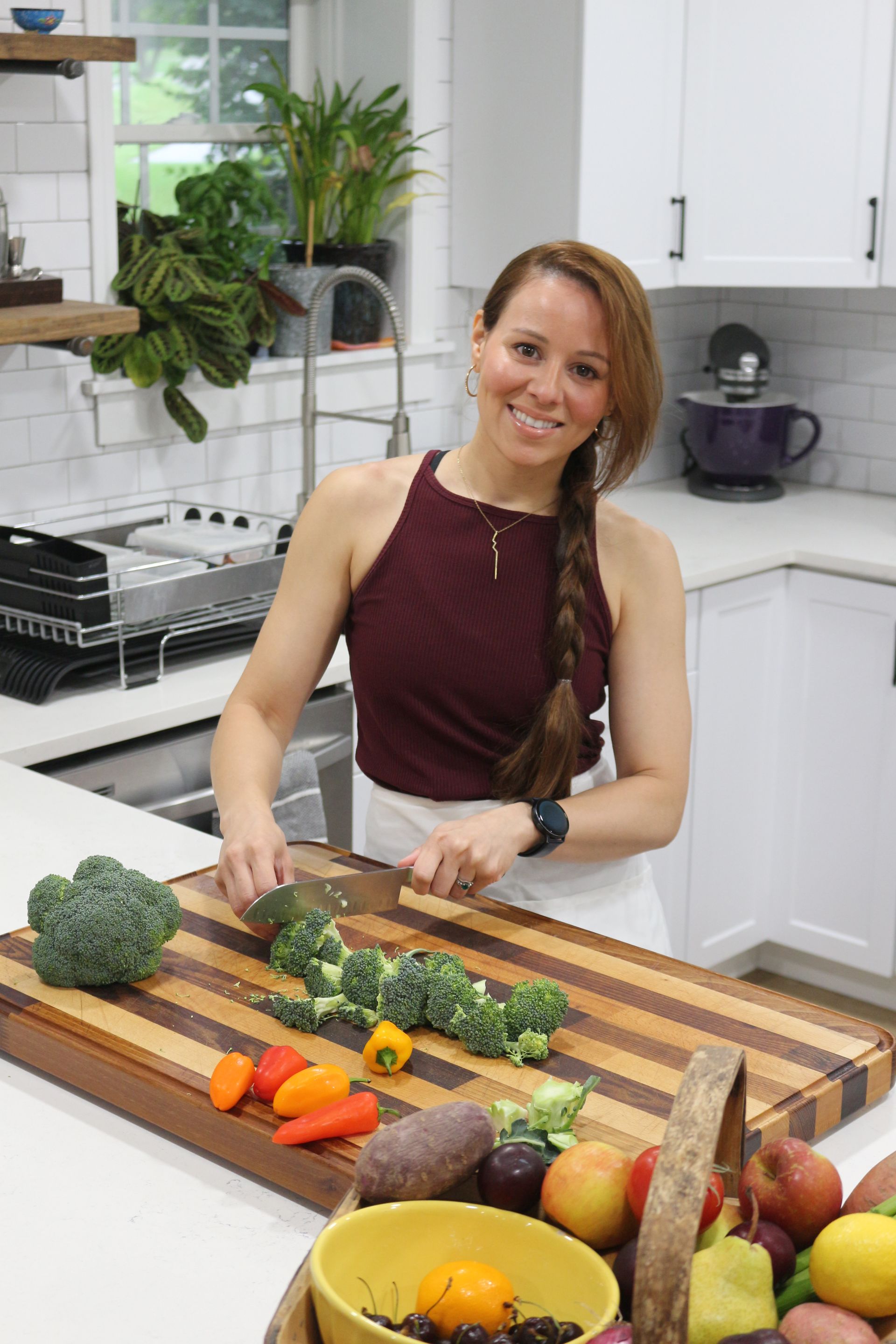 A woman is cutting vegetables on a wooden cutting board in a kitchen.