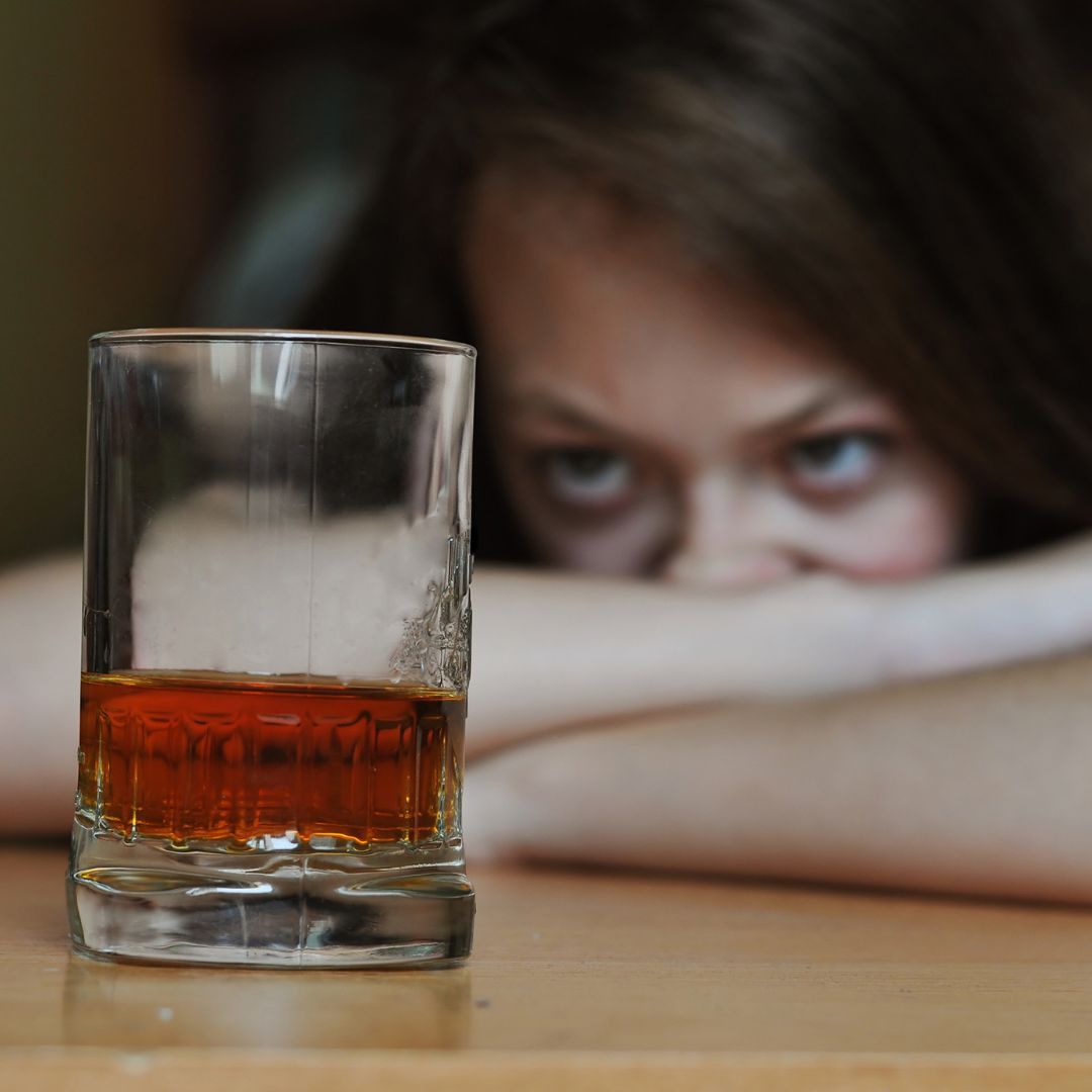 A woman is hiding her face behind a glass of whiskey