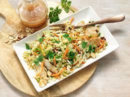 Chicken salad with dressing, carrots, almonds, and cilantro on a white plate atop a wooden board.