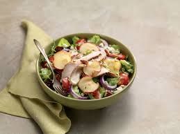 Salad bowl with lettuce, potatoes, red onion, tomatoes, and meat; on a napkin.