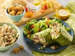 Chicken salad wraps with a side salad and condiments on a table.