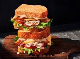 Stacked turkey, bacon, and cheese sandwich on a wooden board.