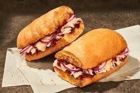 Two sandwiches on parchment paper; filled with meat and red onion on a golden, crusty roll.
