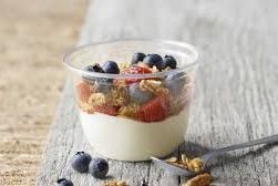 Yogurt parfait with blueberries, granola, and strawberries in a clear plastic cup on a wooden surface.