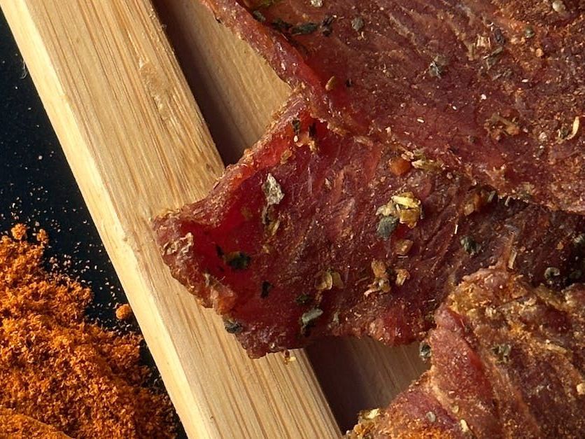 A close up of a piece of jerky on a wooden cutting board