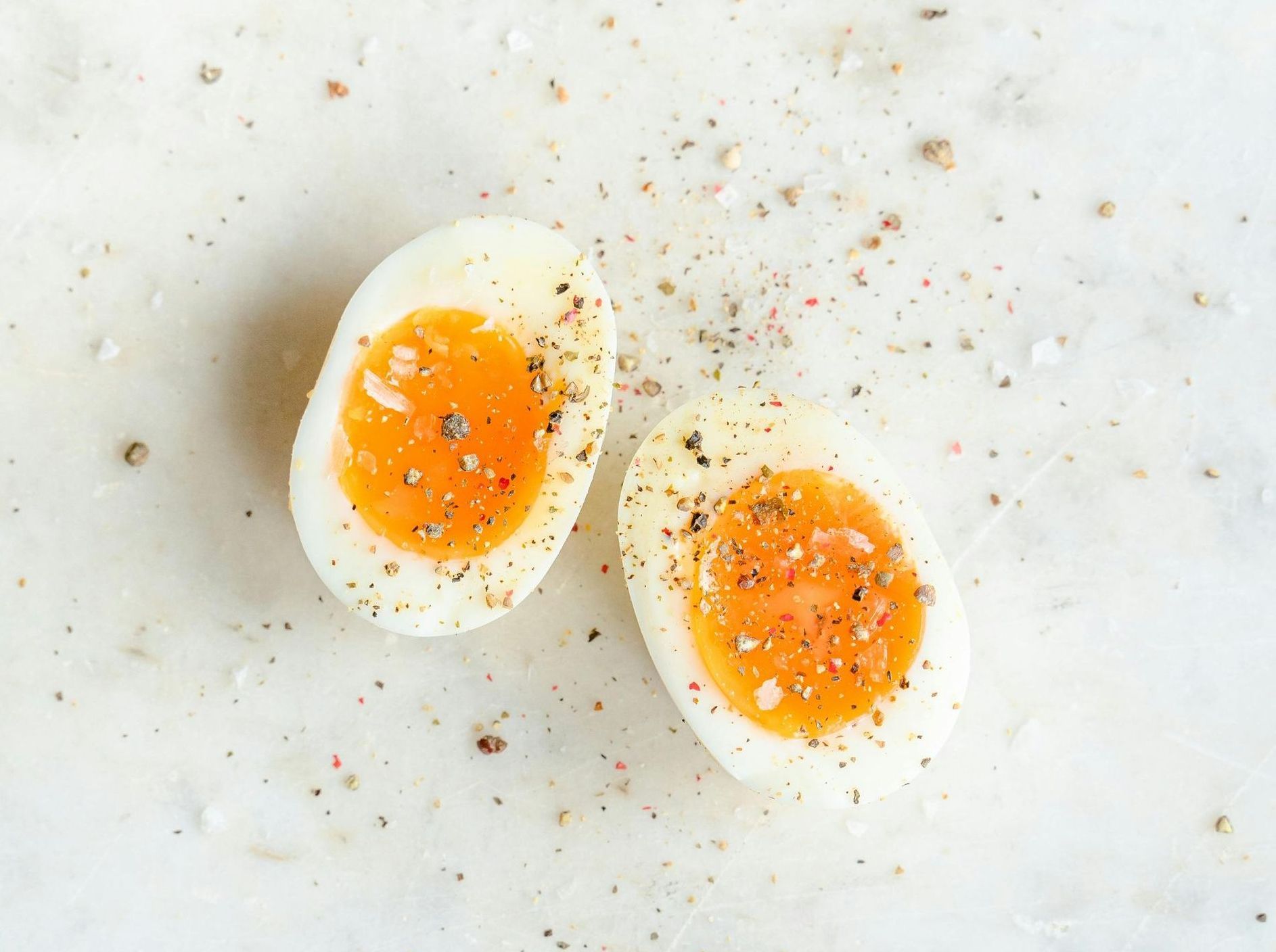 Two halved soft-boiled eggs, yolk visible, sprinkled with salt and pepper on a white surface.