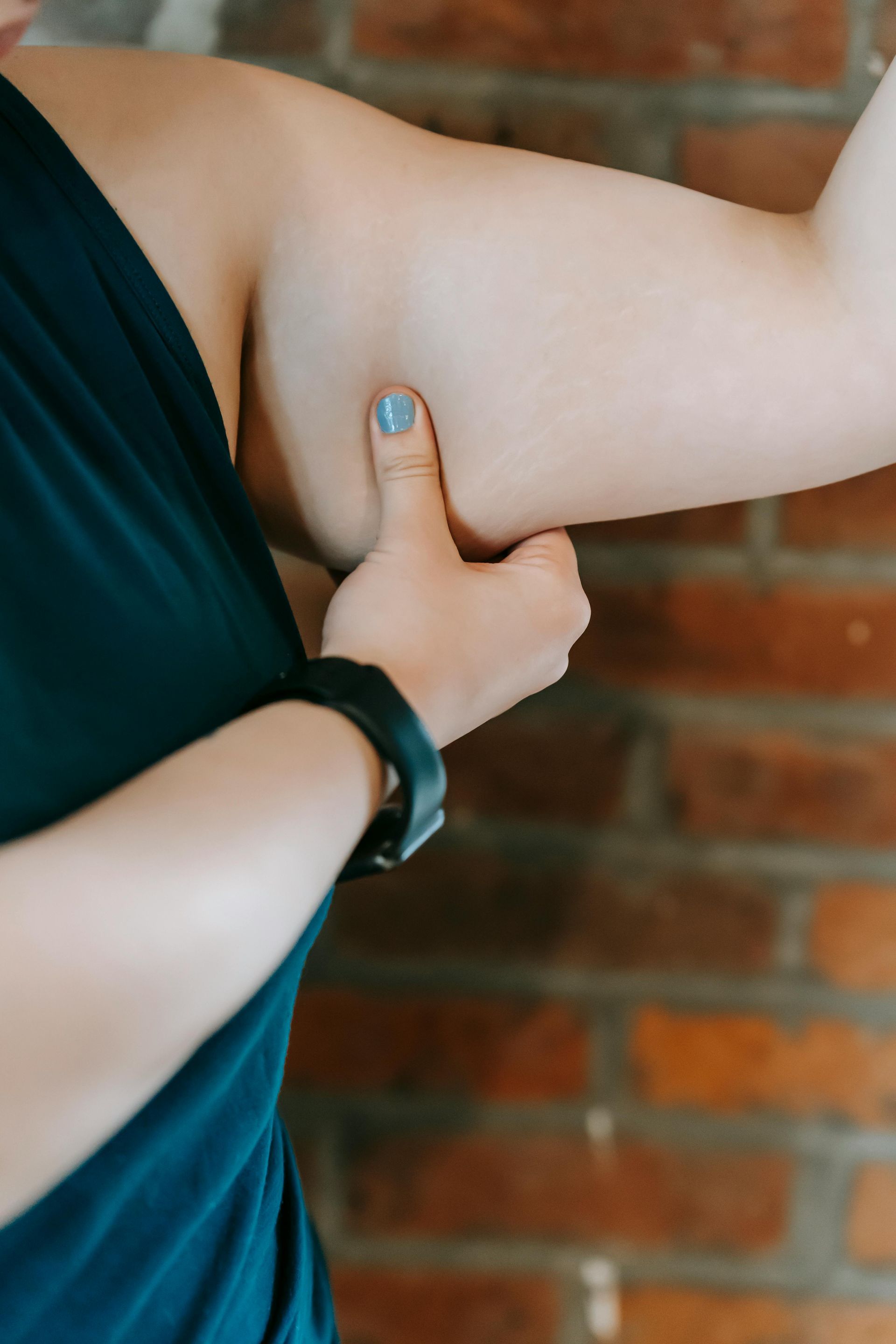 A woman is holding her arm in front of a brick wall.