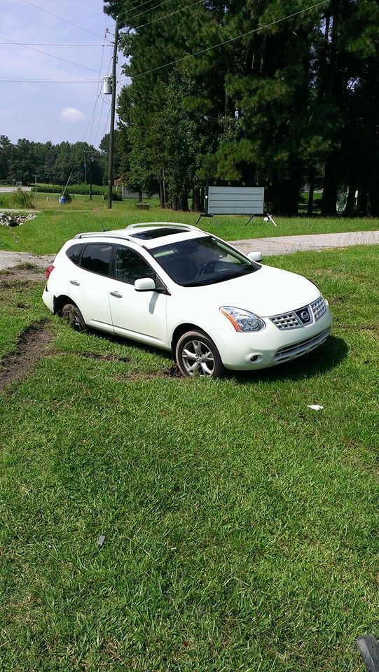 White Nissan SUV stuck in muddy grass field, with open sunroof.