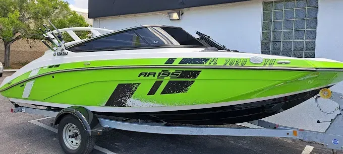 A green and white motorboat on a trailer. The boat has black accents and a tinted windshield.