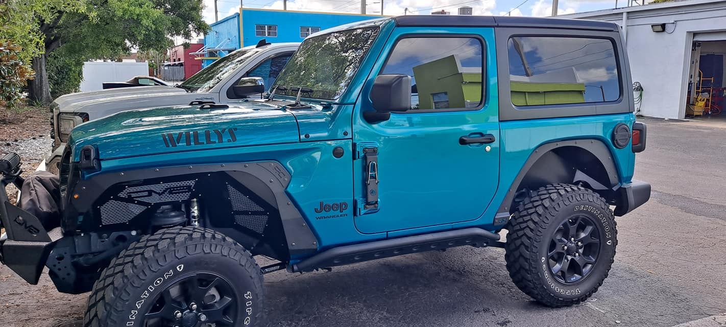 Teal Jeep Wrangler with black wheels and a black hardtop parked on the street.