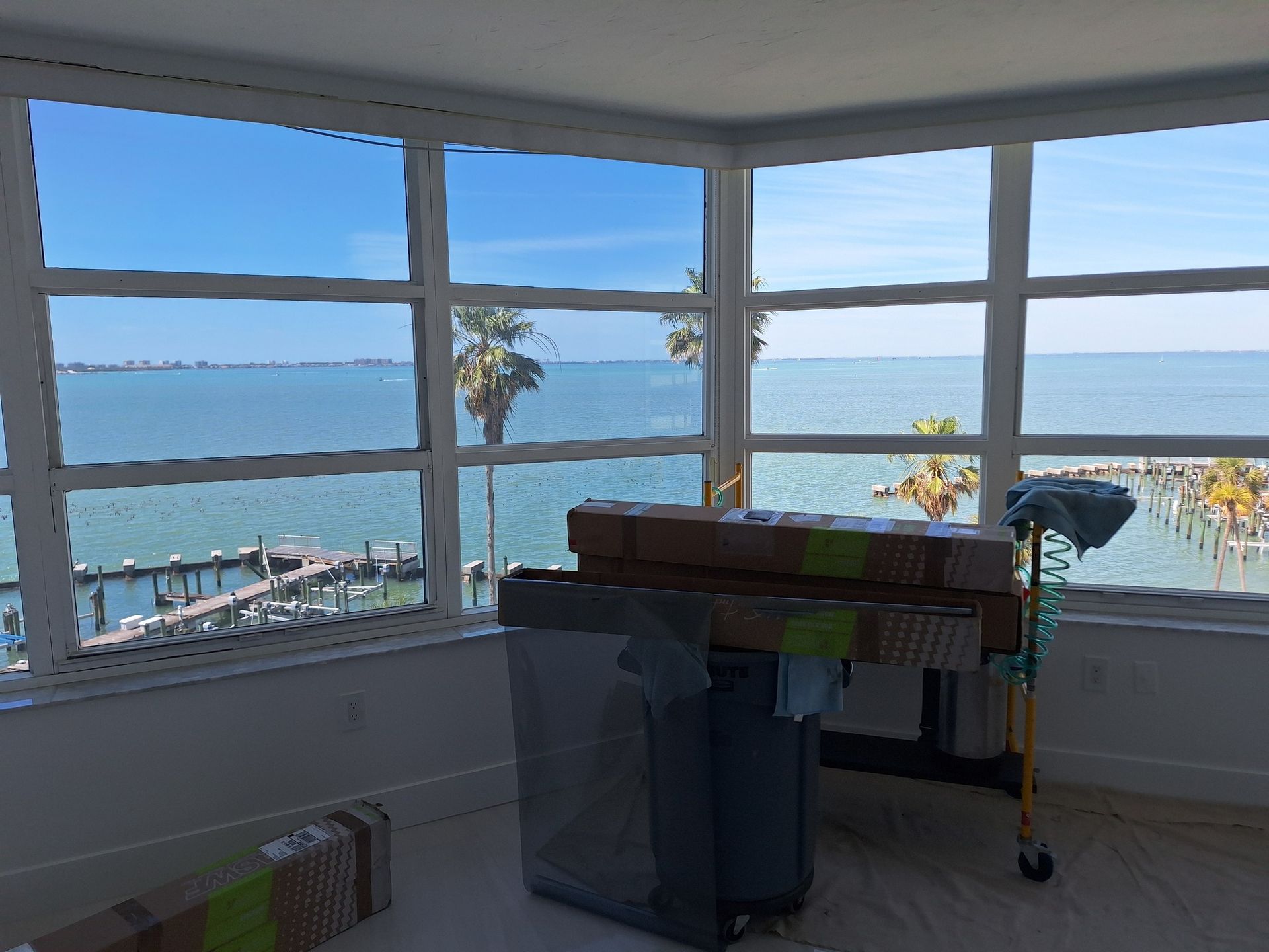 View from a room with large windows overlooking the ocean and palm trees, with a covered grill in the foreground.