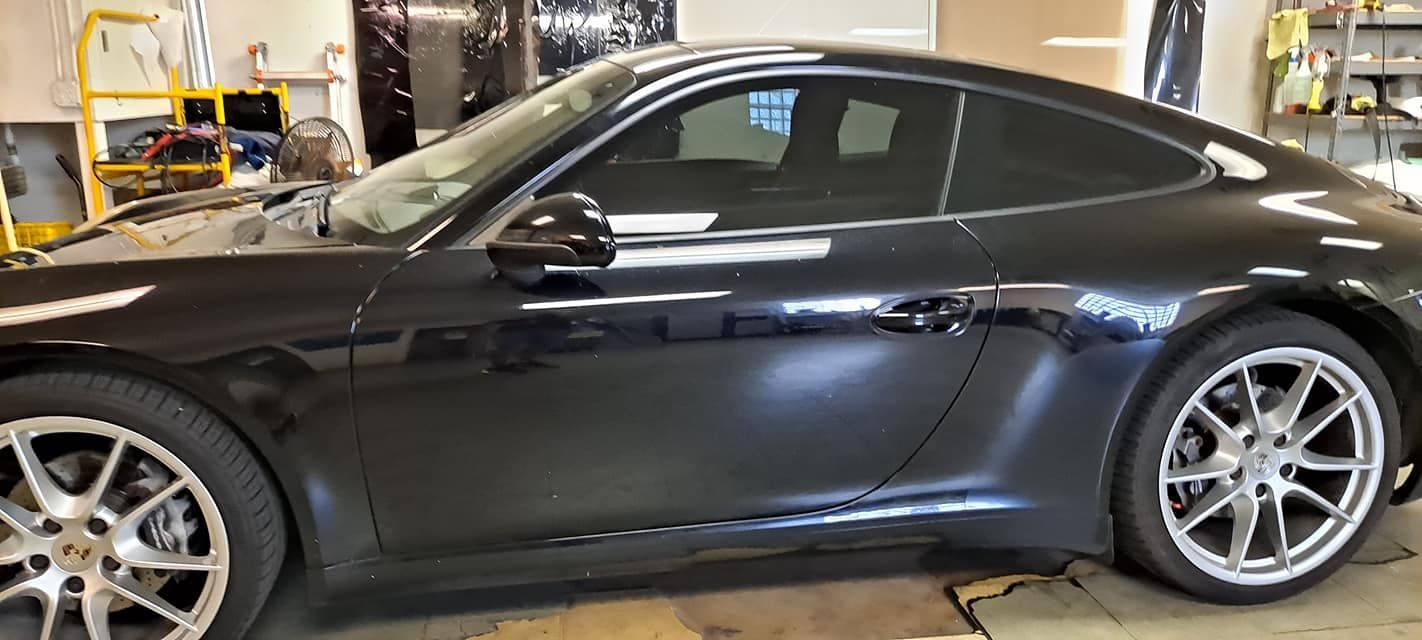 Black Porsche coupe with tinted windows in a garage.