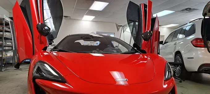 A red McLaren with doors open in a workshop, a white SUV is in the background.