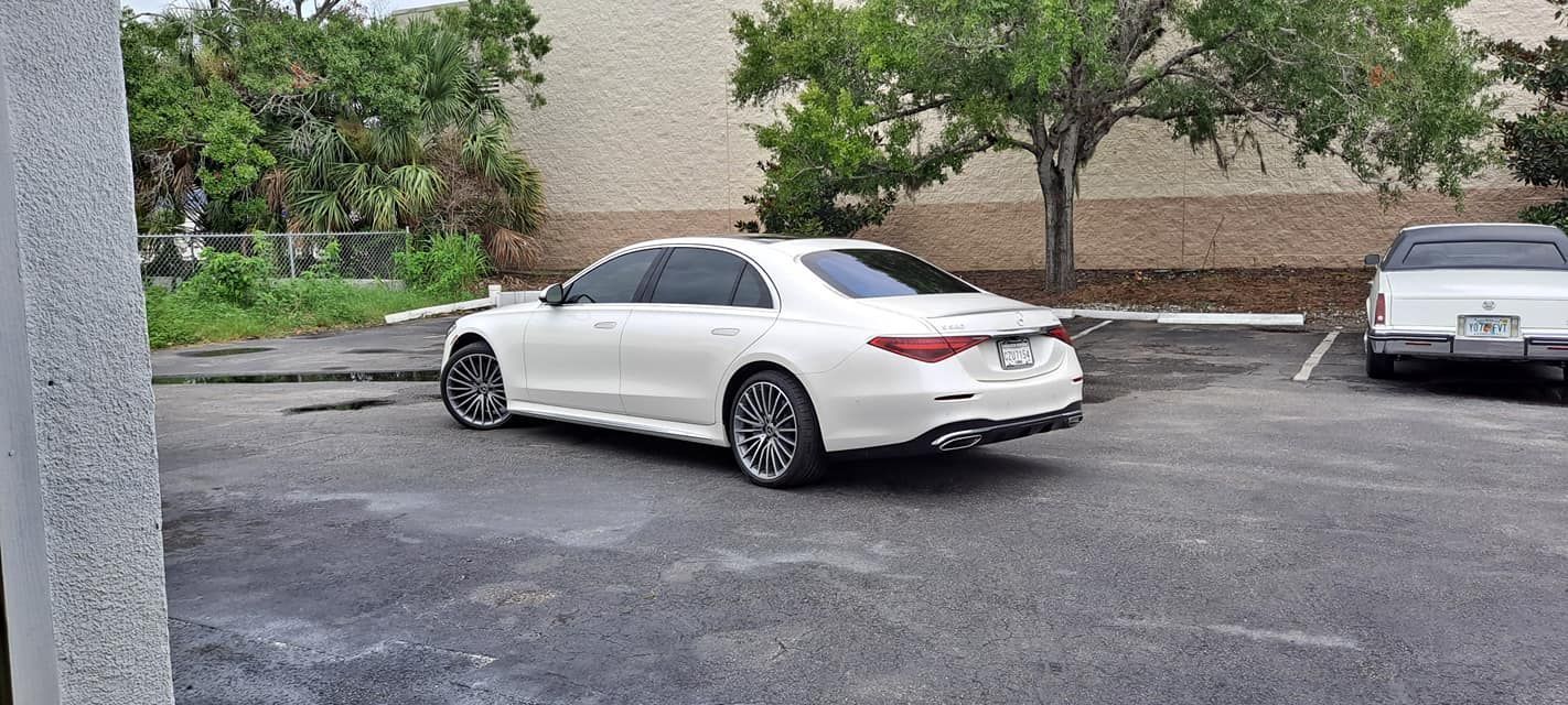 White luxury sedan parked in a parking lot near a building and some trees.