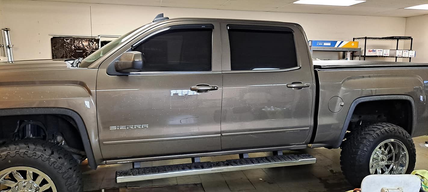 A brown lifted truck with dark tinted windows is parked inside a shop.