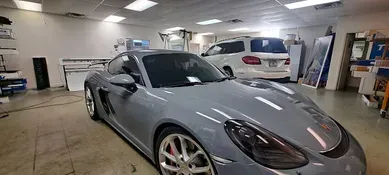 A gray Porsche sports car inside a shop with a white SUV parked behind it.