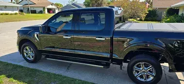 Black Ford F-150 truck parked on a driveway in front of a residential house.
