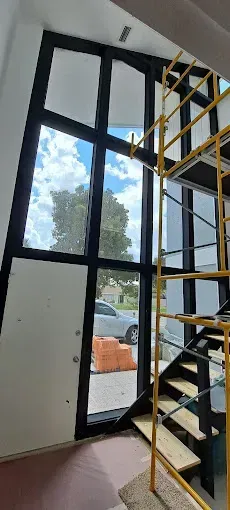 Tall windows with black frames. Staircase and scaffolding inside a building with view to outside.