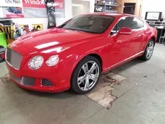 Red Bentley coupe parked in a garage, chrome accents, shiny wheels.