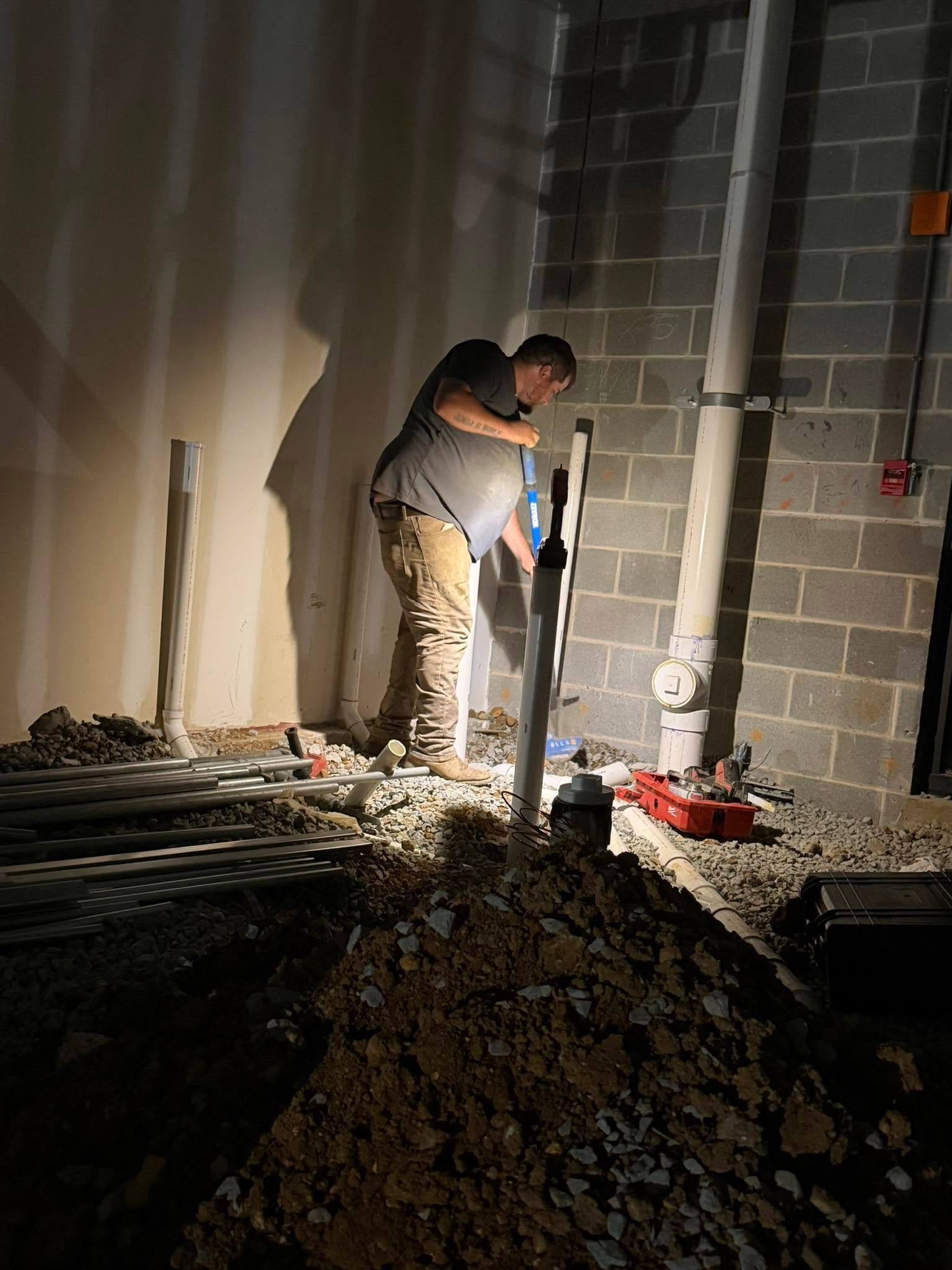 Worker digging a trench indoors with a shovel beside cinder block walls and construction debris