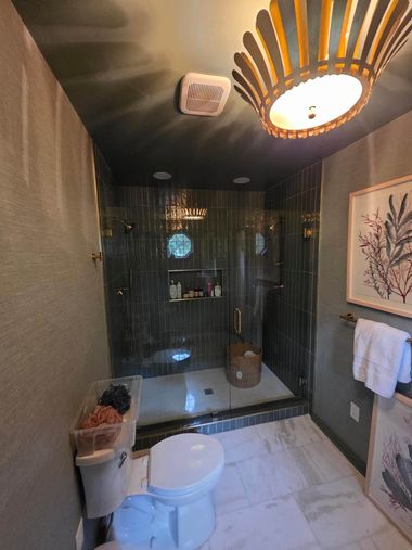 Modern bathroom with white toilet, glass shower, dark walls, and gold pendant light