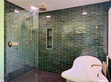 Green-tiled bathroom with glass shower enclosure and white tub chair