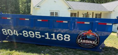 Blue Cardinal dumpster with phone number in front of a house and trees
