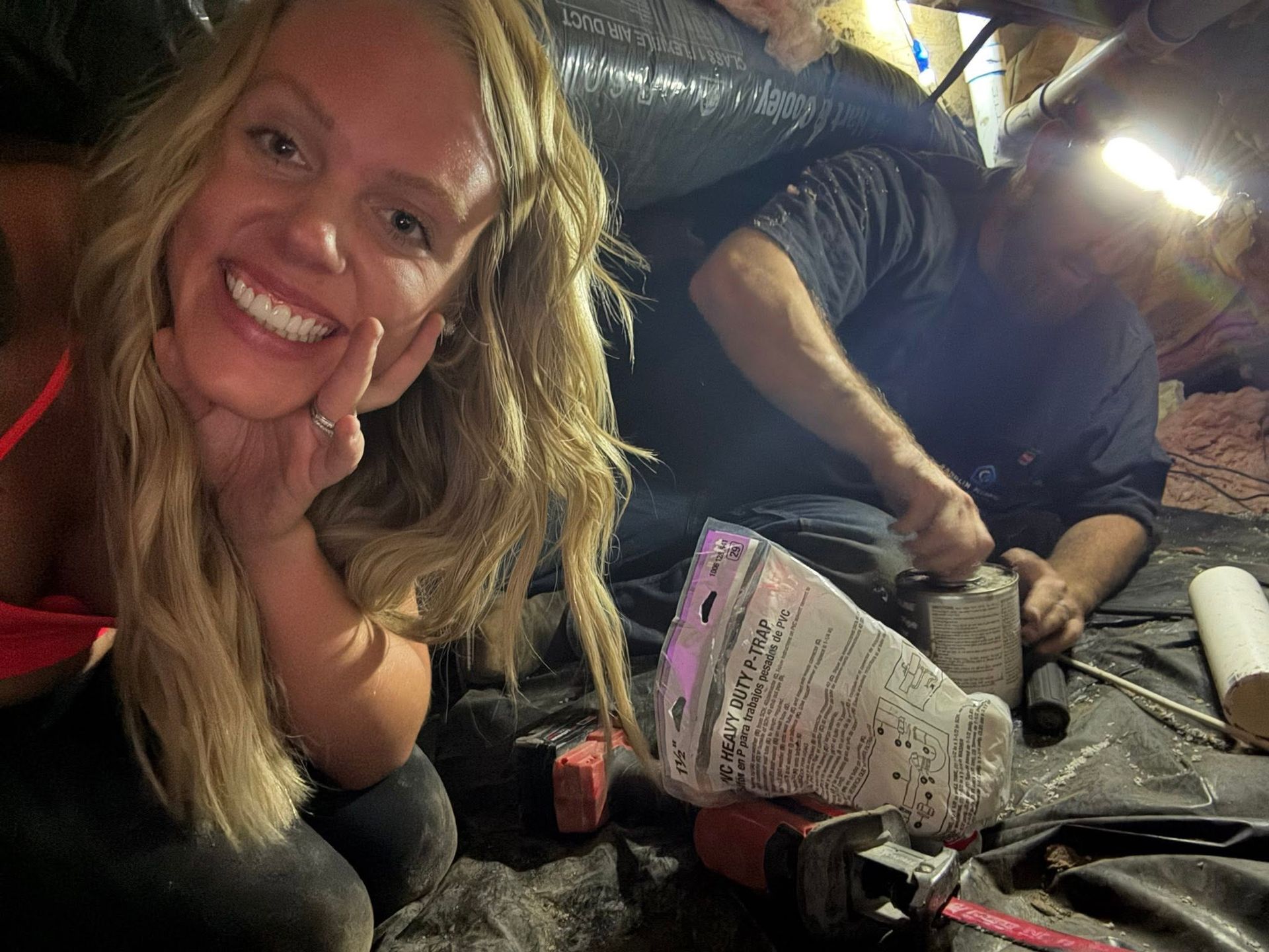 Smiling woman leaning toward the camera in a dim tent, with two people working in the background.