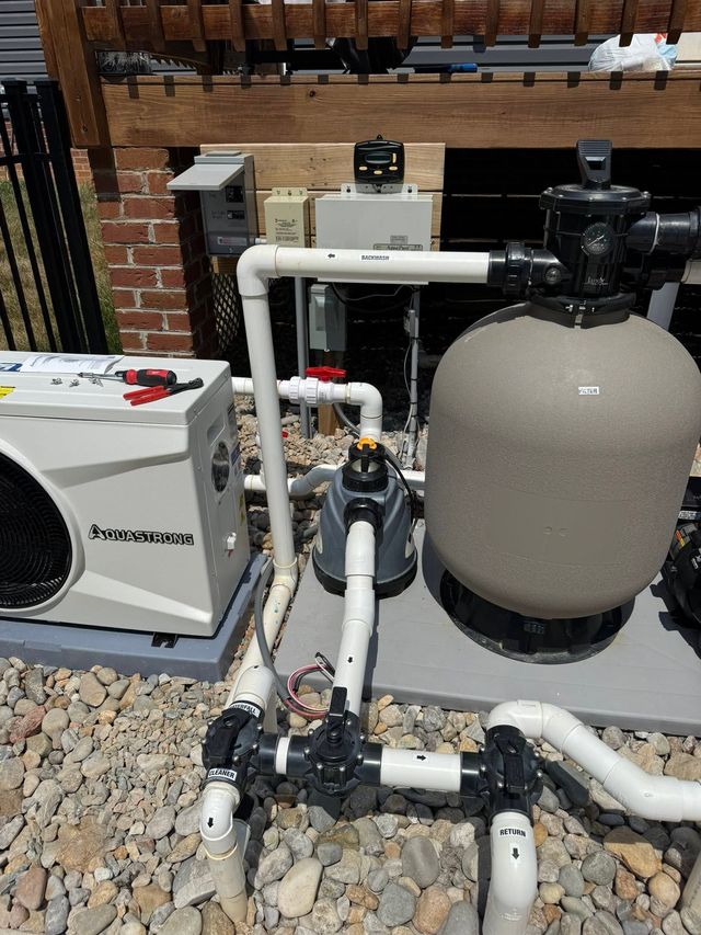 Pool pump and filtration equipment with white pipes, a large gray tank, and a generator in a gravel yard.