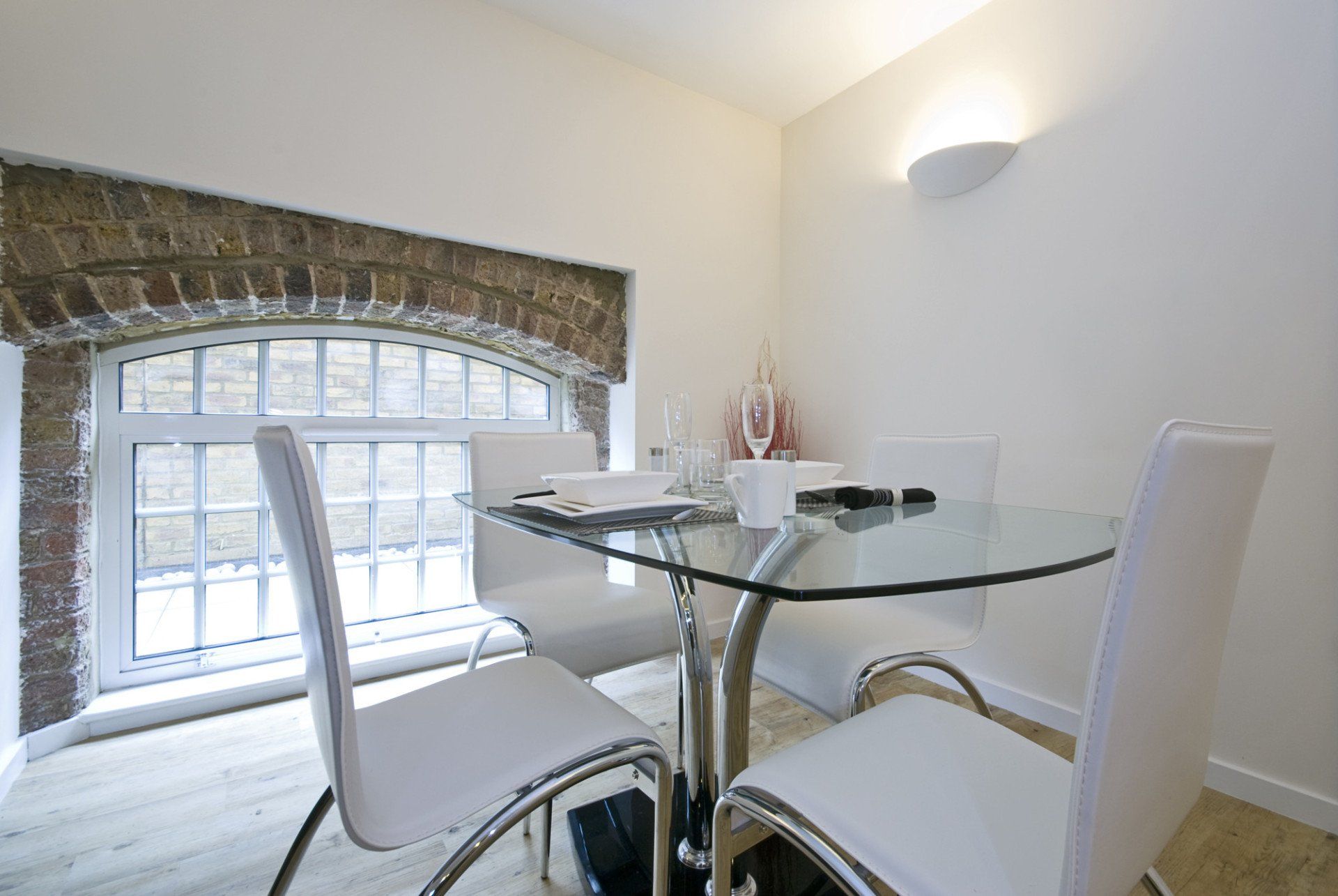 Bright dining area with a round glass table, white chairs, and a large window