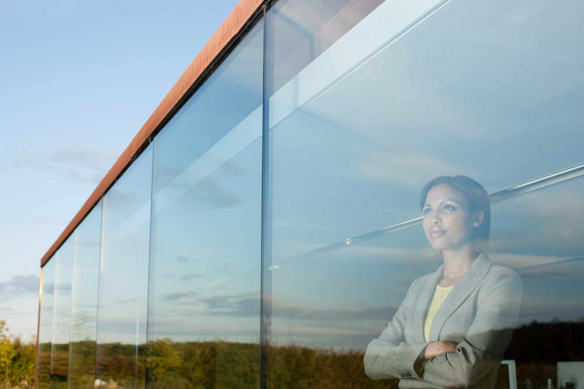 Person standing behind large floor-to-ceiling glass windows on a modern building