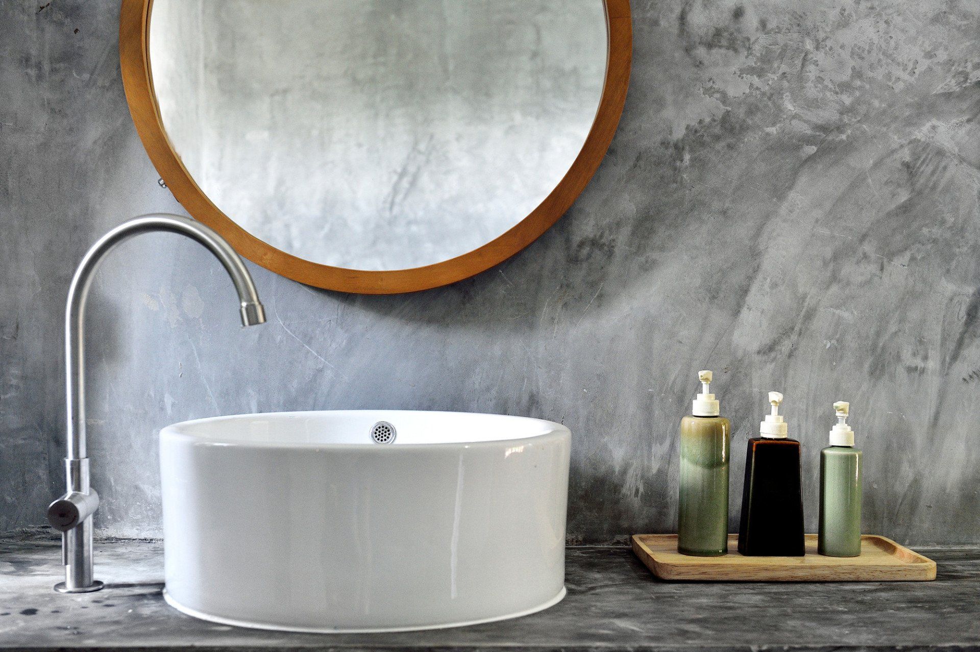 Modern bathroom featuring a round mirror, vessel sink, and textured gray wall