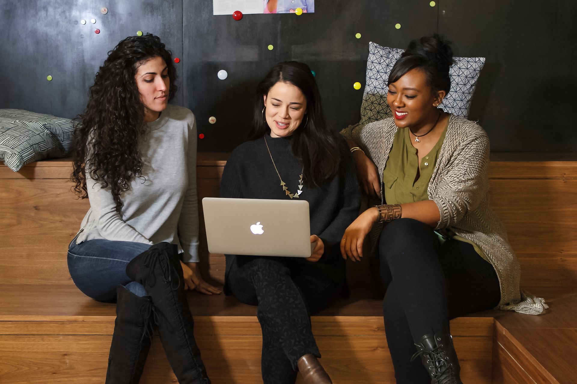 Three people sit on a couch, smiling at a laptop in a cozy room.