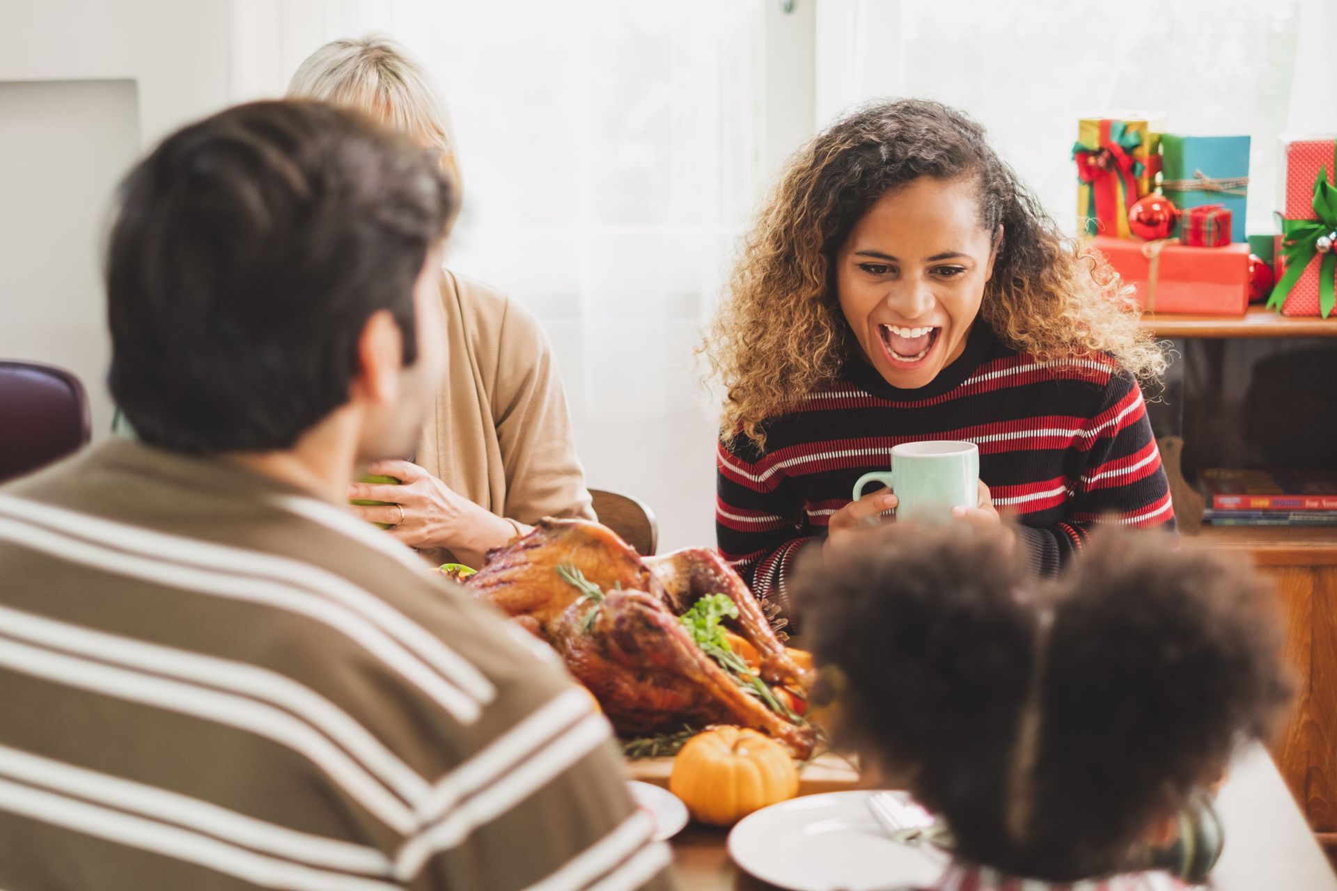 People gathered around a table, smiling and sharing food in a festive, warmly lit room.