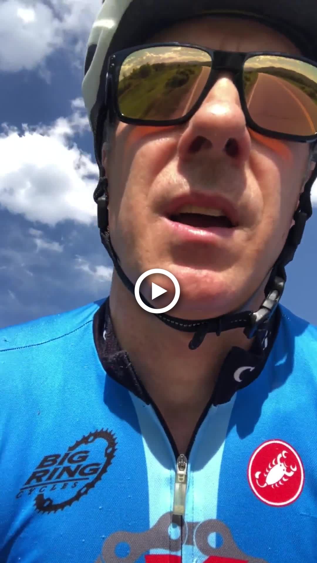 Close-up of a cyclist in a blue jersey and helmet against a bright cloudy sky