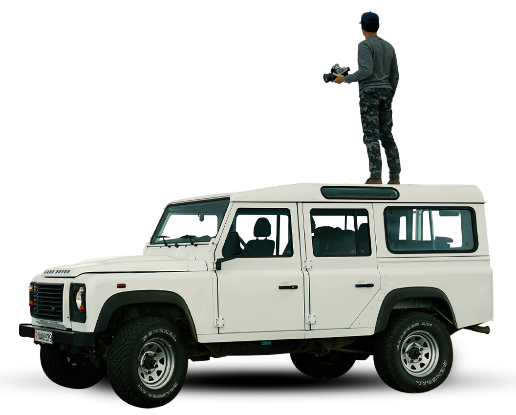 White SUV with a person standing on the roof holding equipment on a plain background