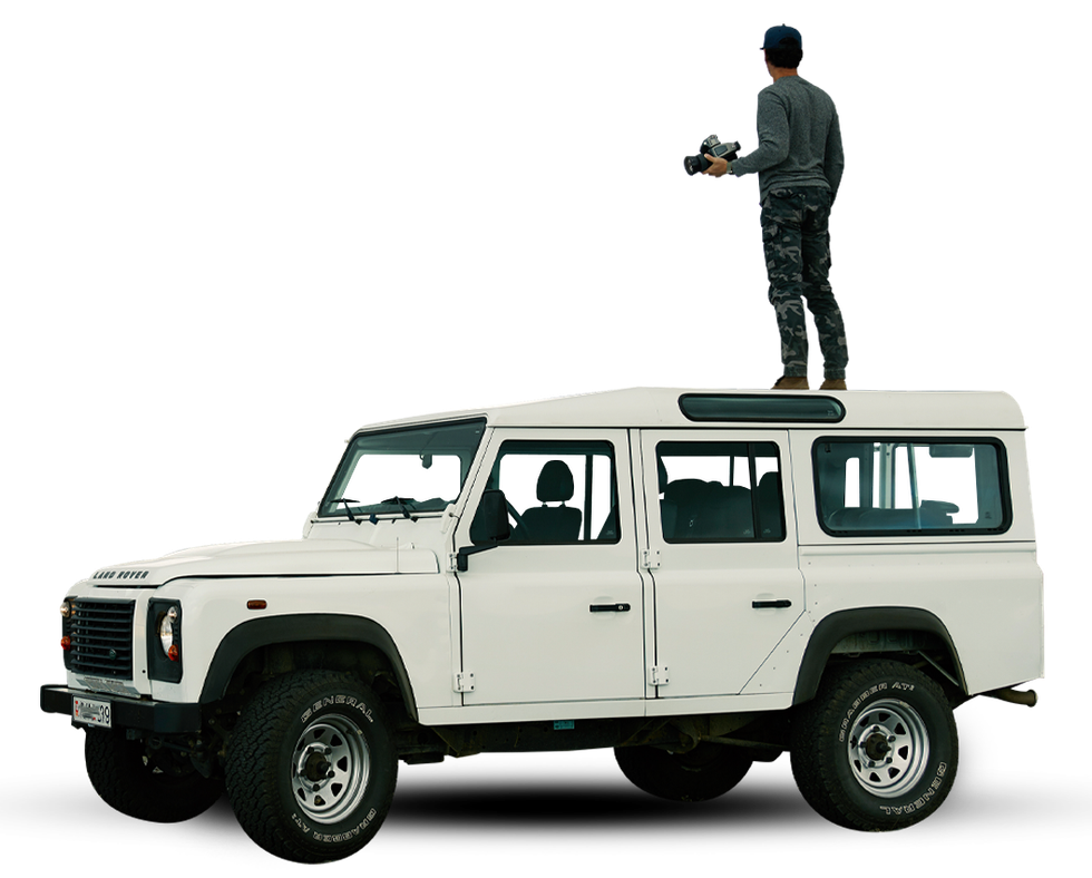 White SUV with a person standing on the roof holding equipment on a plain background