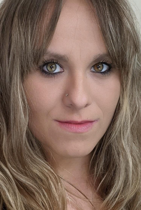 Close-up portrait of a person with long blonde hair, blue eyes, and a slight smile on a light background