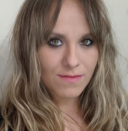 Close-up portrait of a person with long wavy hair and neutral expression against a light background