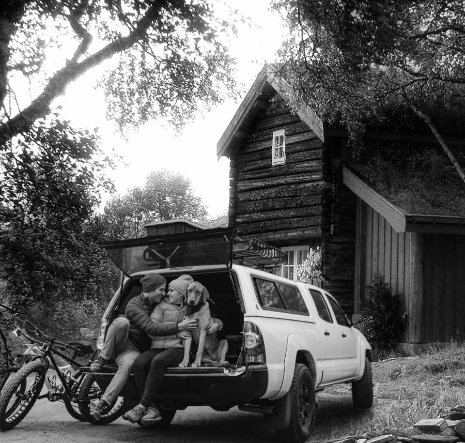 Bicyclist and dog resting beside a white wagon outside a rustic wooden cabin in the woods