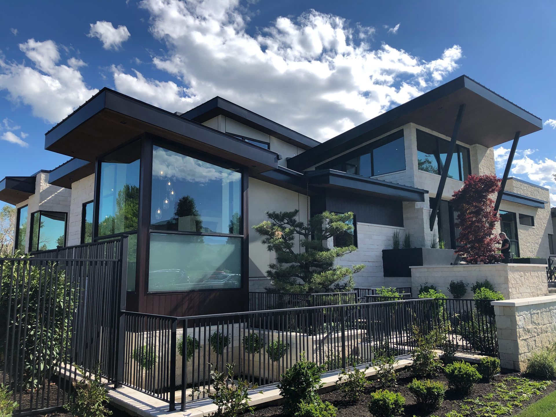 Modern house with large windows, black fence, and landscaped front yard under a bright sky