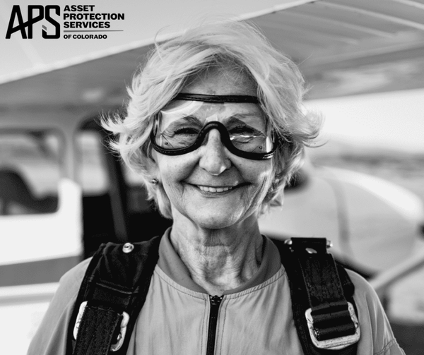 Smiling person wearing goggles and a parachute harness at an airport or skydiving facility