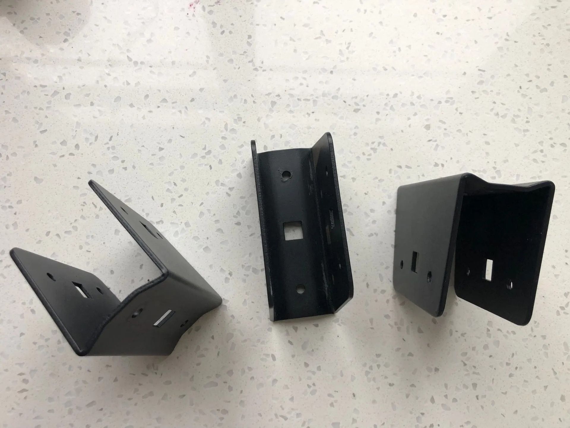 Three black, U-shaped metal mounting brackets for a railing system displayed on a white speckled surface.