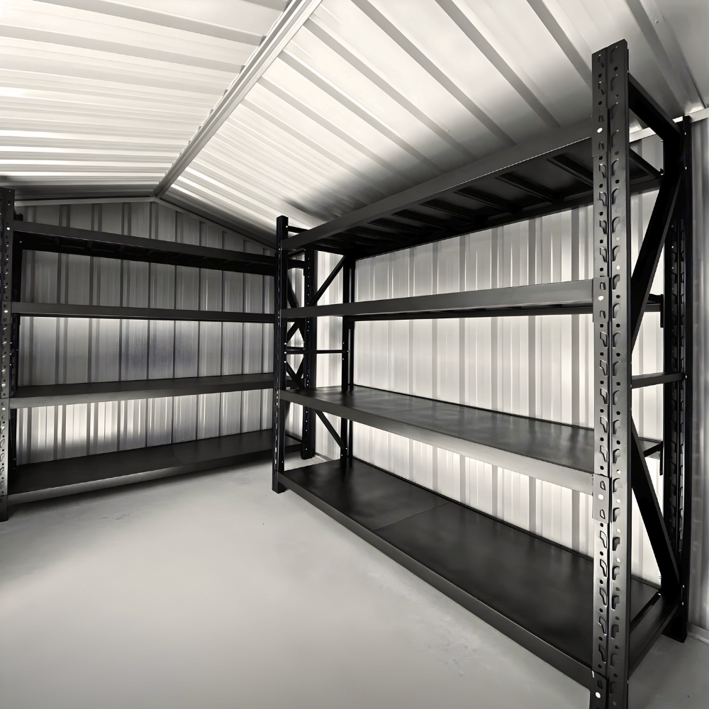 Two black industrial shelving units stand against the corrugated metal walls of an empty storage shed.