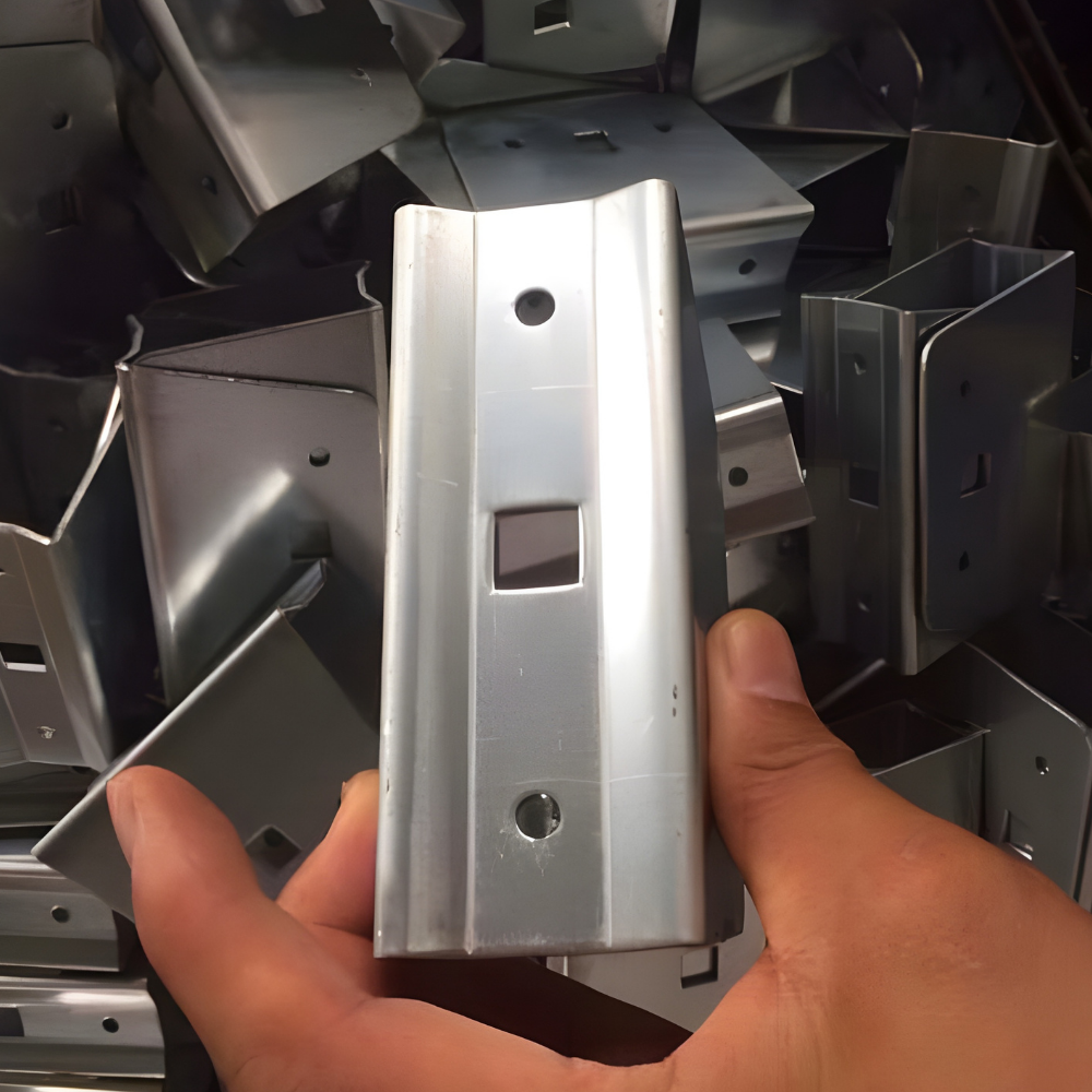 A person's hand holding a silver, U-shaped metal bracket with a square hole and two circular bolt holes.