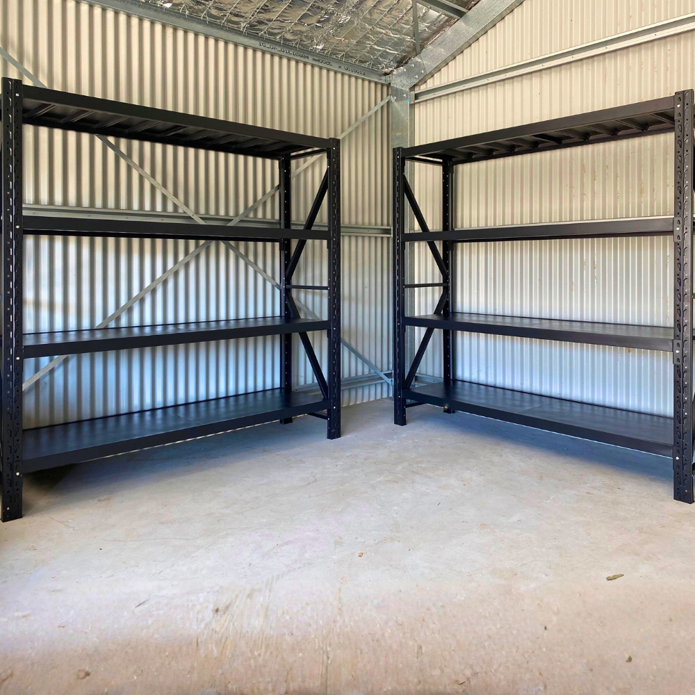 Two tall, black metal shelving units with four tiers each, standing on a concrete floor against a corrugated metal wall.